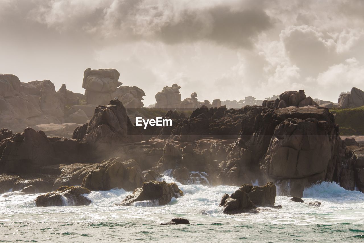 Rock formations by sea against cloudy sky