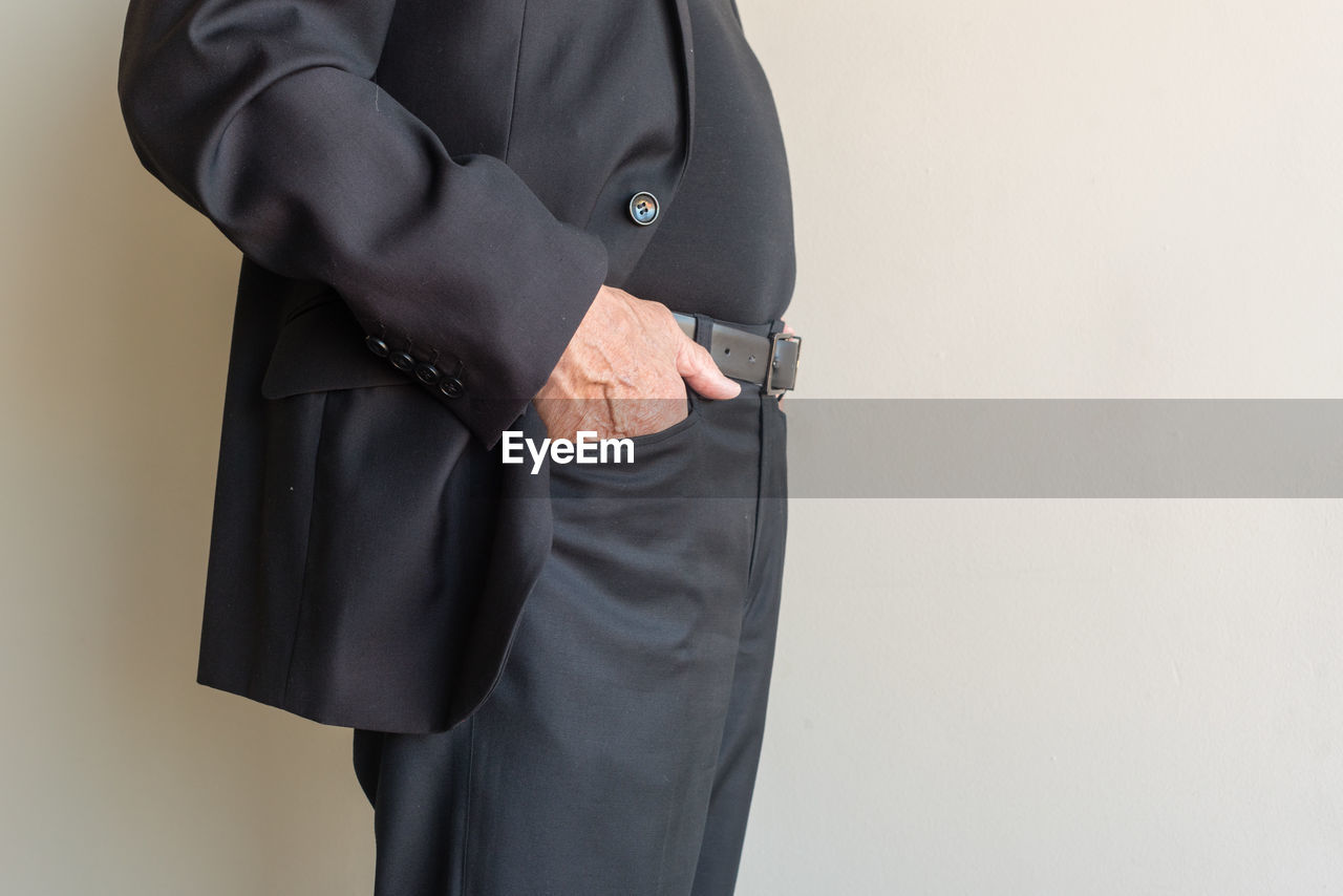 Midsection of man with hands in pockets standing against wall