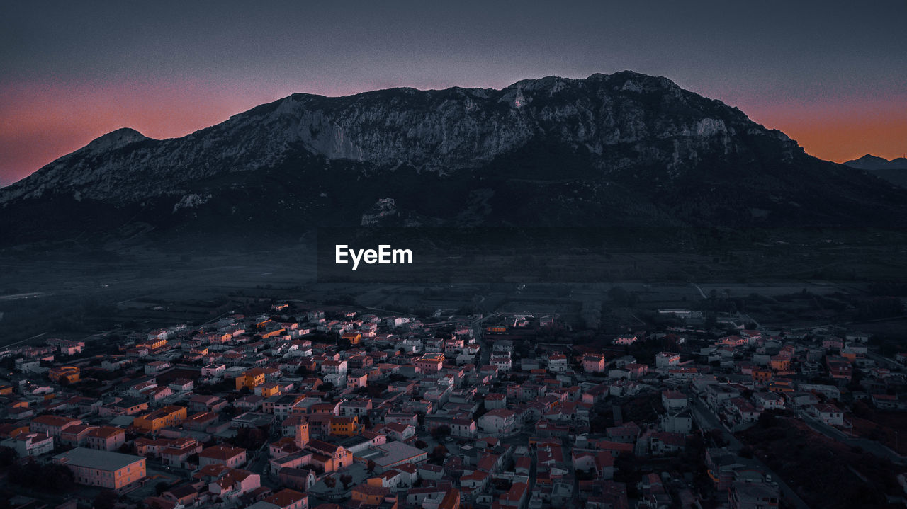 Aerial view of townscape by mountains against sky at sunset
