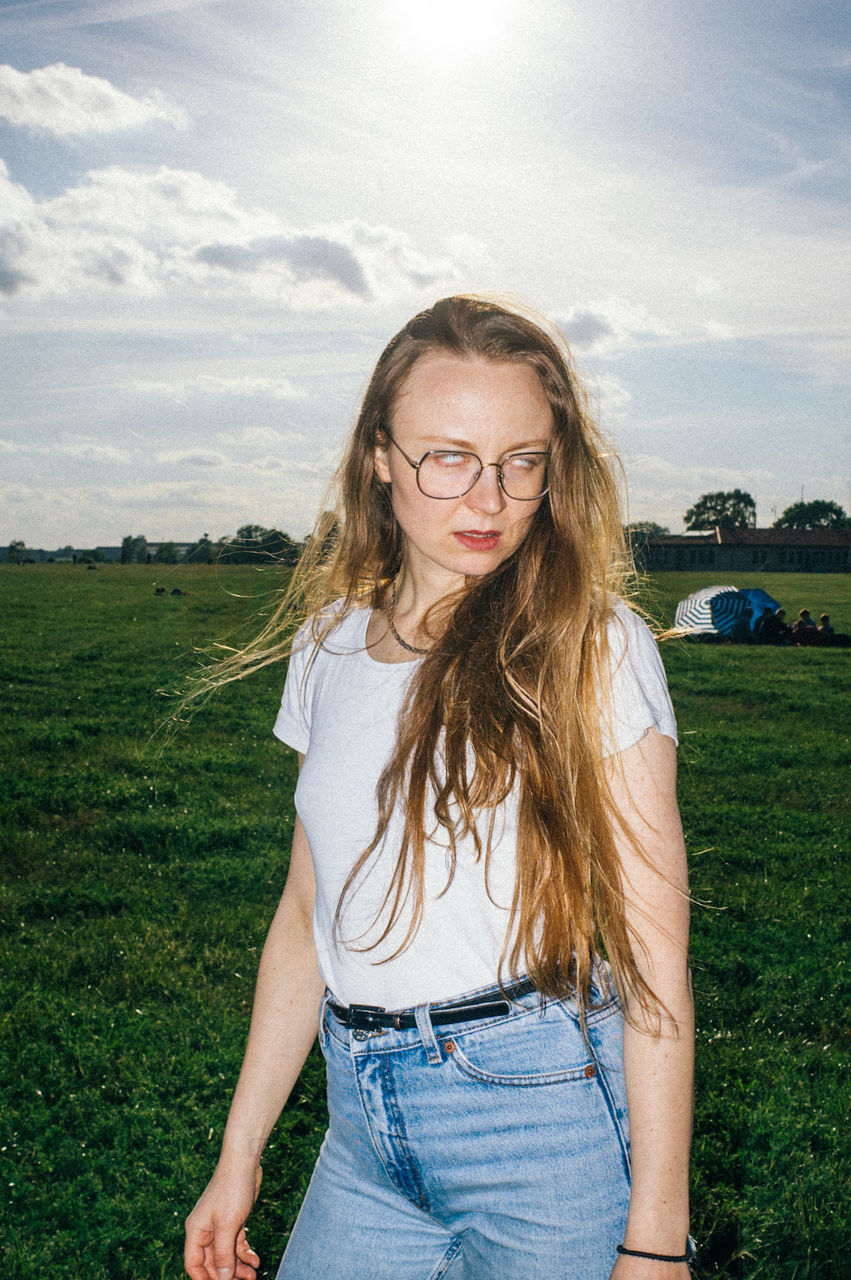 PORTRAIT OF BEAUTIFUL YOUNG WOMAN STANDING ON FIELD