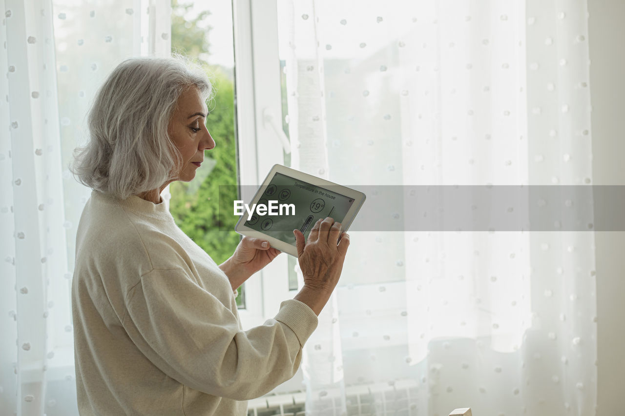 Senior woman adjusting temperature on smart home device