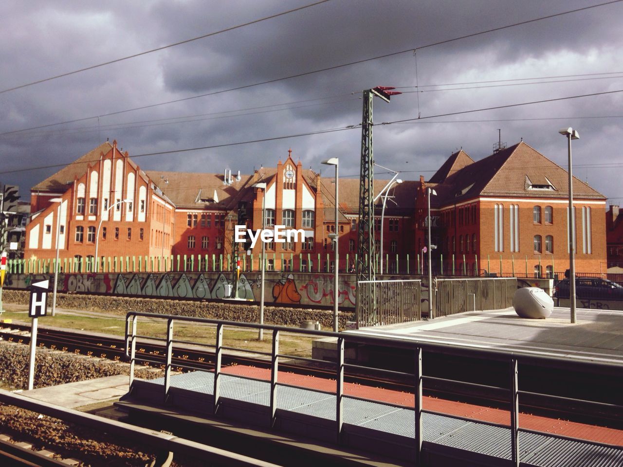 Railroad station platform by houses against cloudy sky