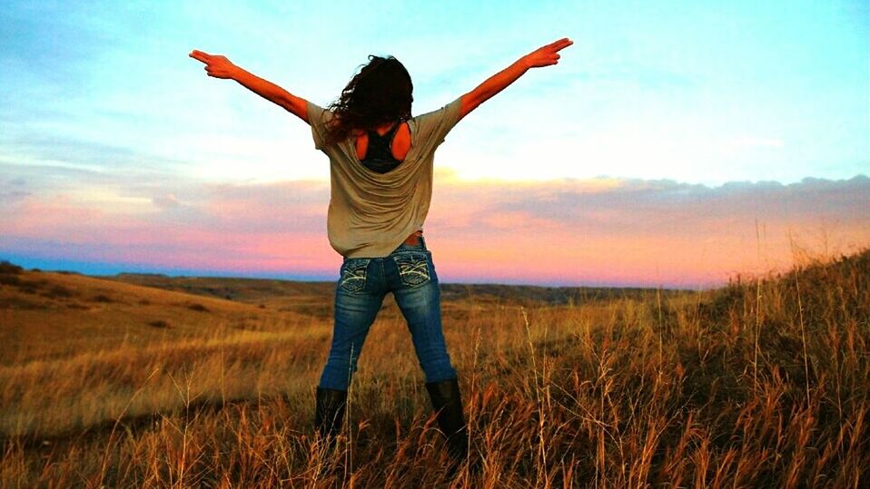 sky, one person, arm, limb, landscape, nature, environment, land, human limb, arms raised, arms outstretched, field, adult, prairie, sunset, grass, beauty in nature, plant, happiness, horizon, casual clothing, emotion, rural scene, standing, women, leisure activity, scenics - nature, cloud, natural environment, young adult, positive emotion, carefree, grassland, lifestyles, outdoors, sunlight, tranquility, full length, vacation, enjoyment, child, joy, cheerful, smiling, holiday, trip, vitality, mountain, tranquil scene, rear view, non-urban scene, copy space, idyllic, summer, relaxation, three quarter length