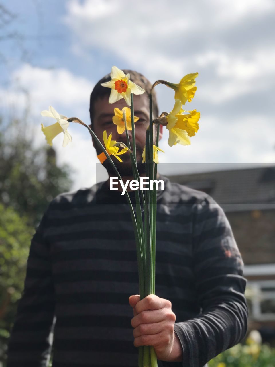 Low angle view of man holding yellow flowers against cloudy sky