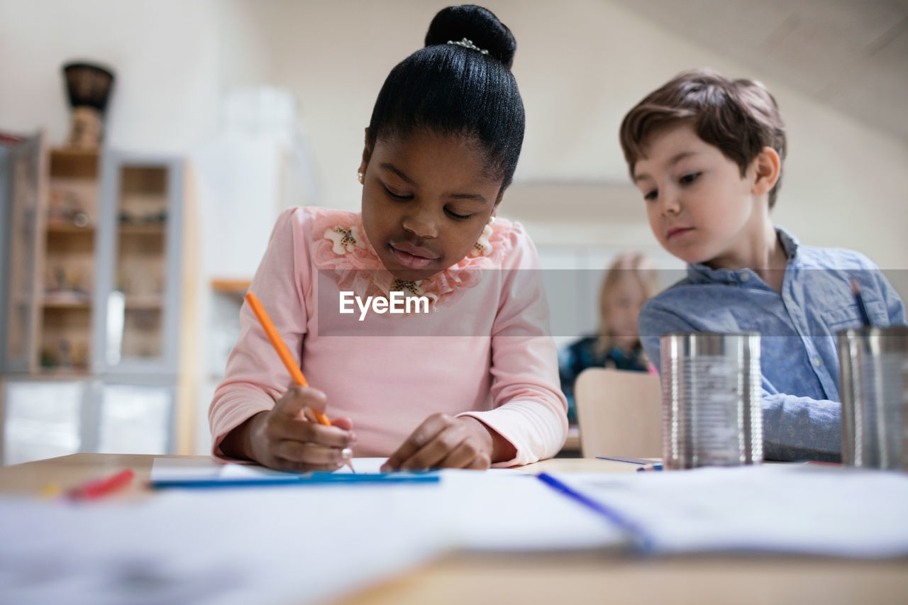 Boy in friend's paper while studying in classroom at table