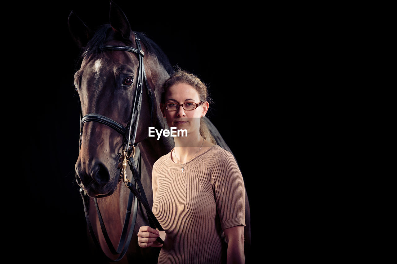 Portrait of confident woman with horse standing against black background