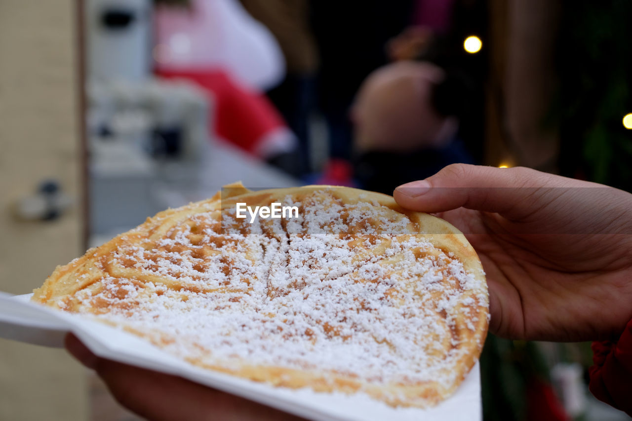 Close-up two hands holding one big tasty waffle with icing sugar. santa at advent christmas market. 