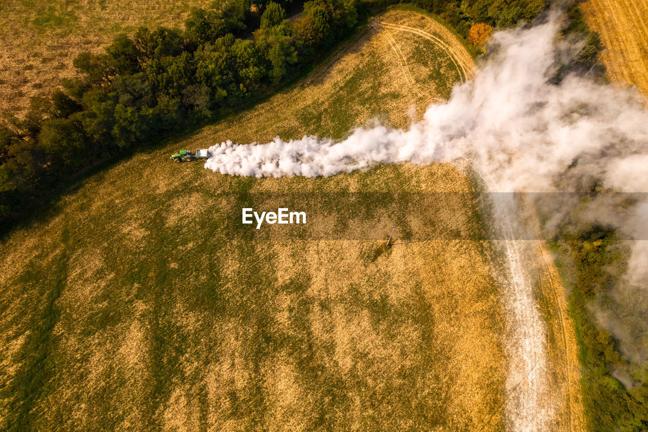 Aerial view of a tractor spreading lime on fields to improve soil quality after the harvest. 