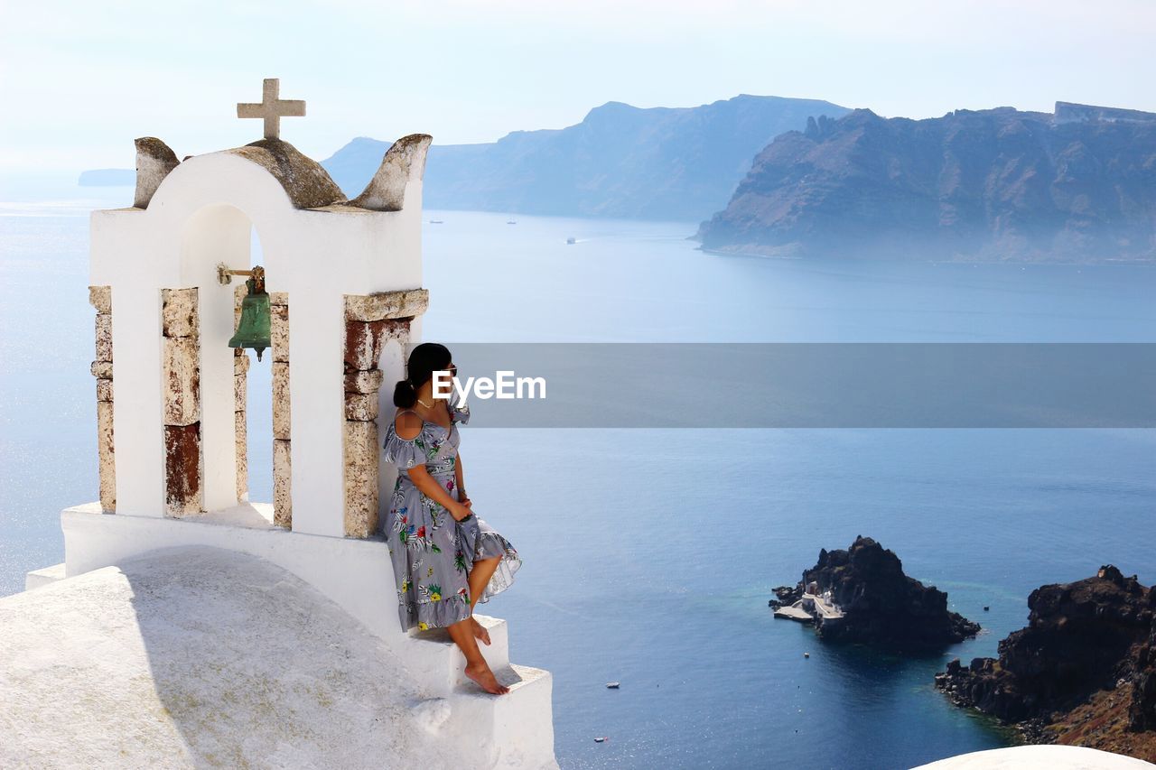Woman leaning by cross against sea at santorini