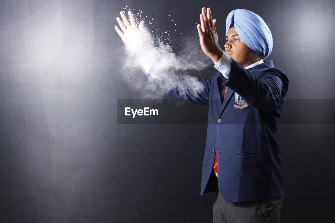 Side view of teenage boy dusting hands while standing against gray background