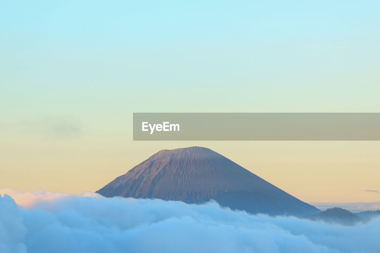 Scenic view of mountain and clouds against clear sky during sunset