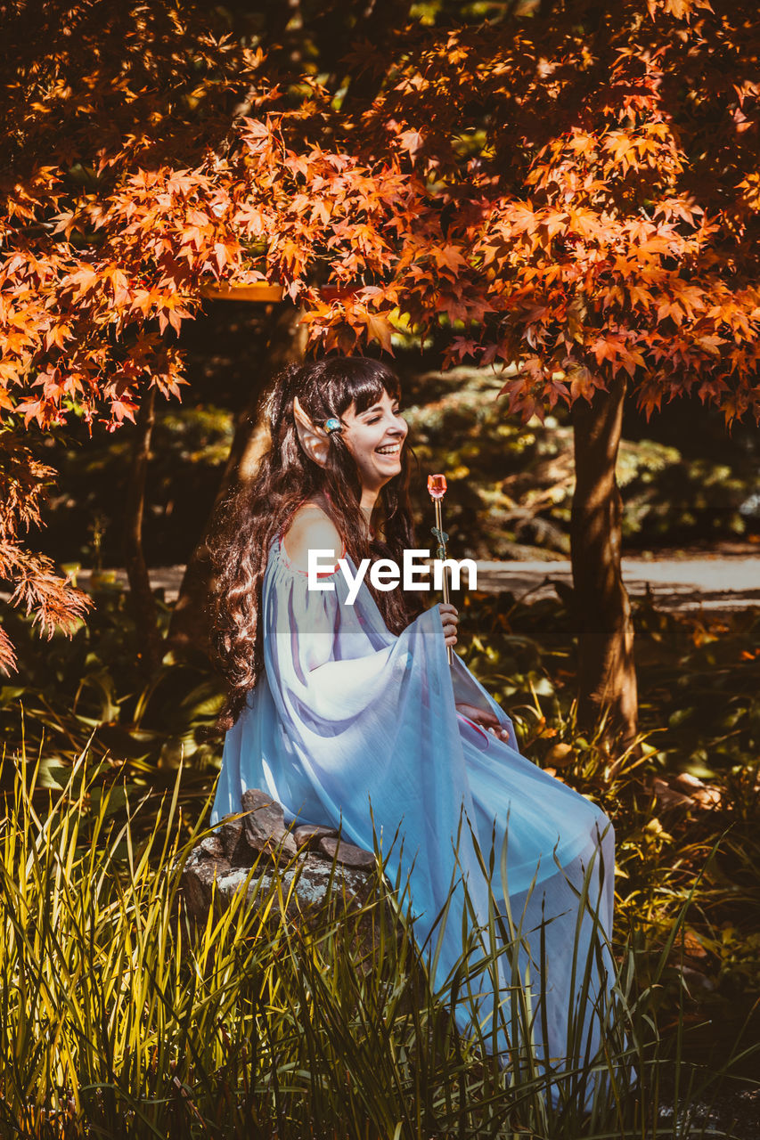 Young woman sitting against tree during autumn