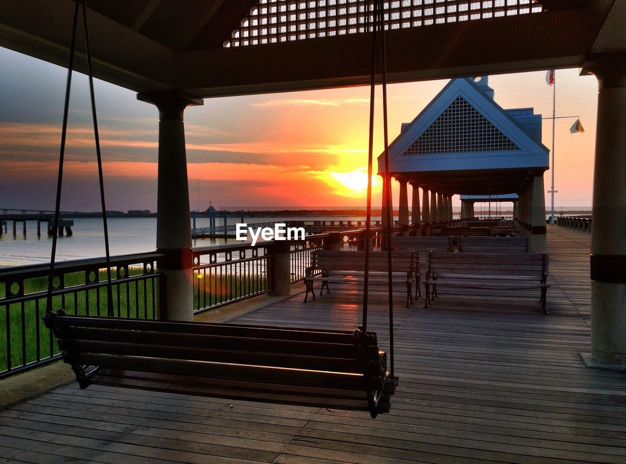 Swing and benches on hardwood floor at waterfront park during sunrise