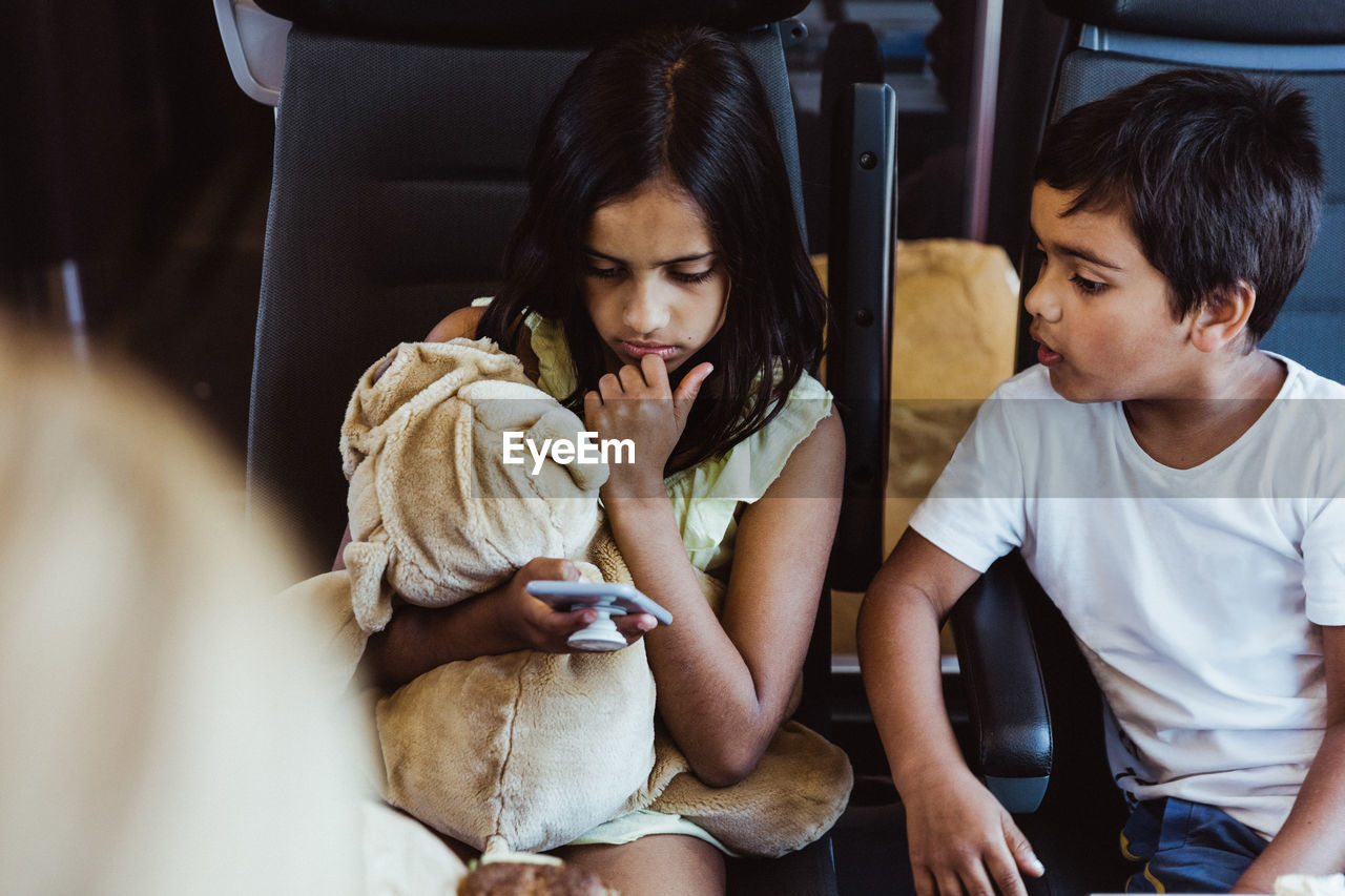 Boy looking at sister using smart phone while traveling in train