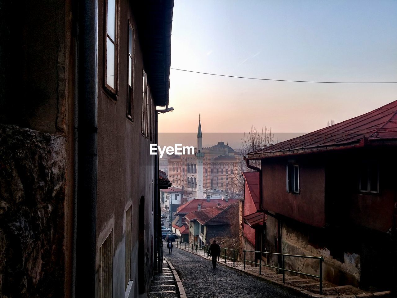 Street amidst houses against sky at sunset