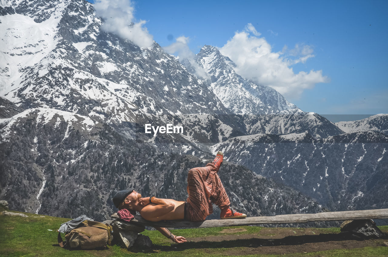 Man relaxing on bench against sky