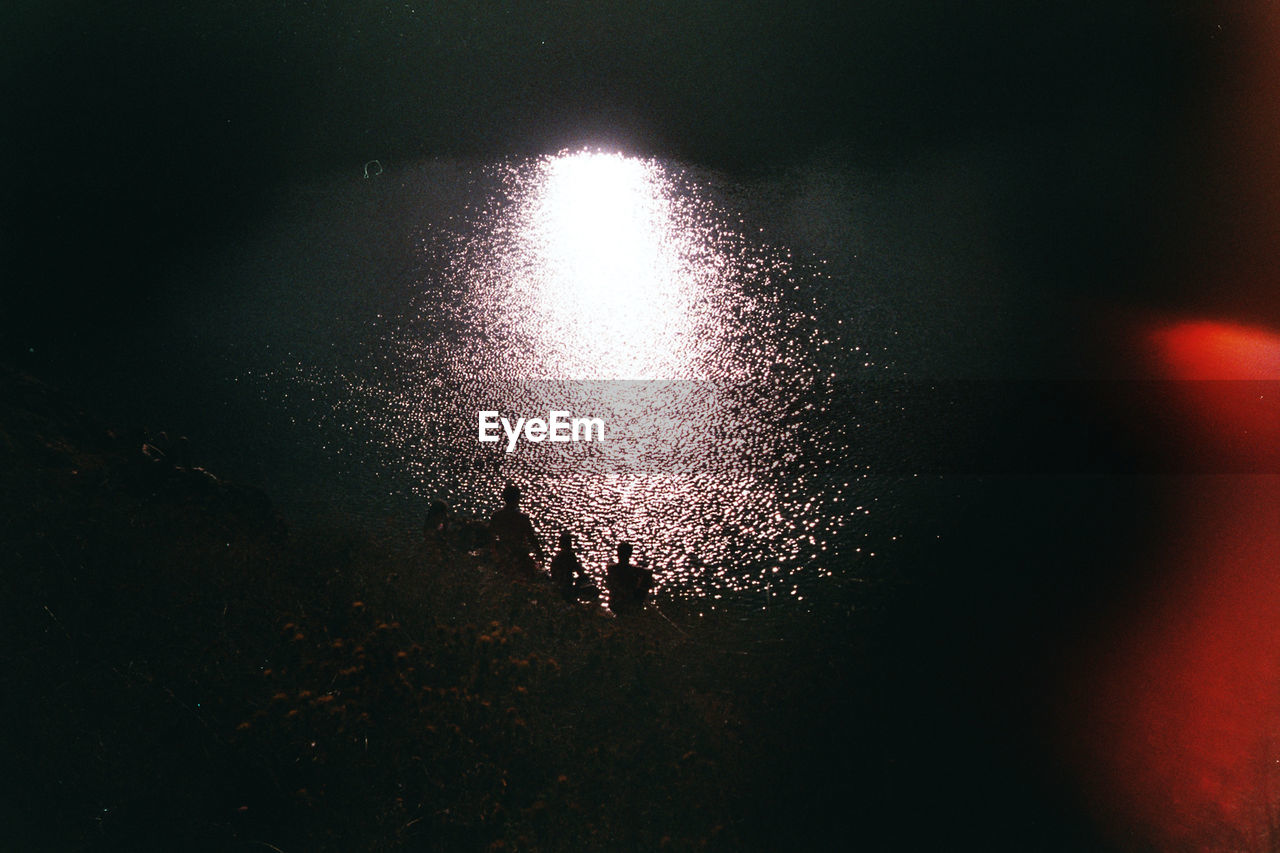 High angle view of silhouette people sitting by sea at night