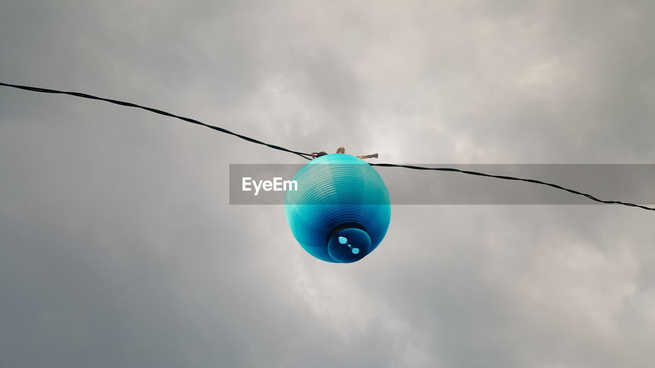 Low angle view of lantern hanging on cable against cloudy sky