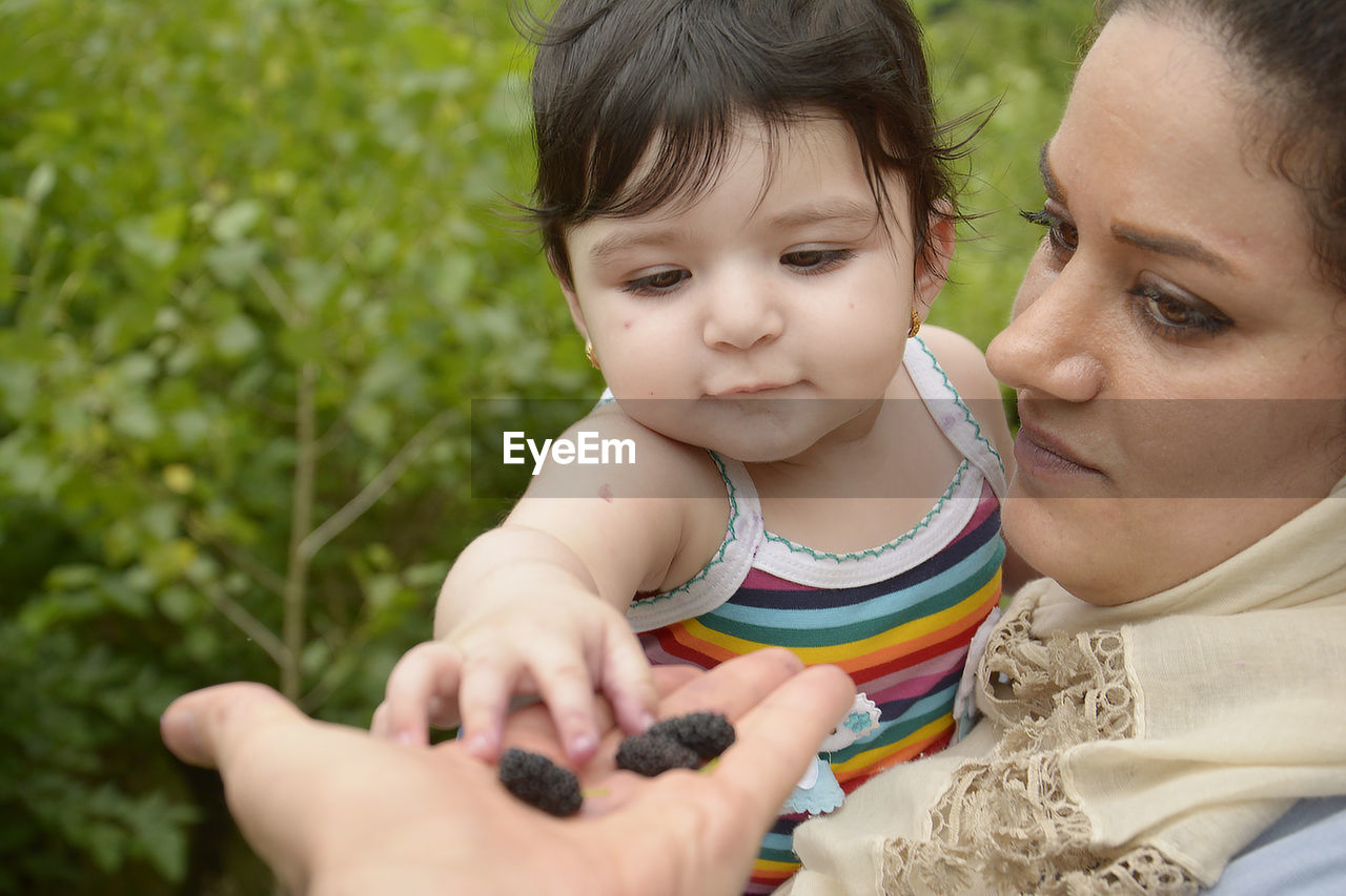 Mother holding fruit while carrying daughter on field 