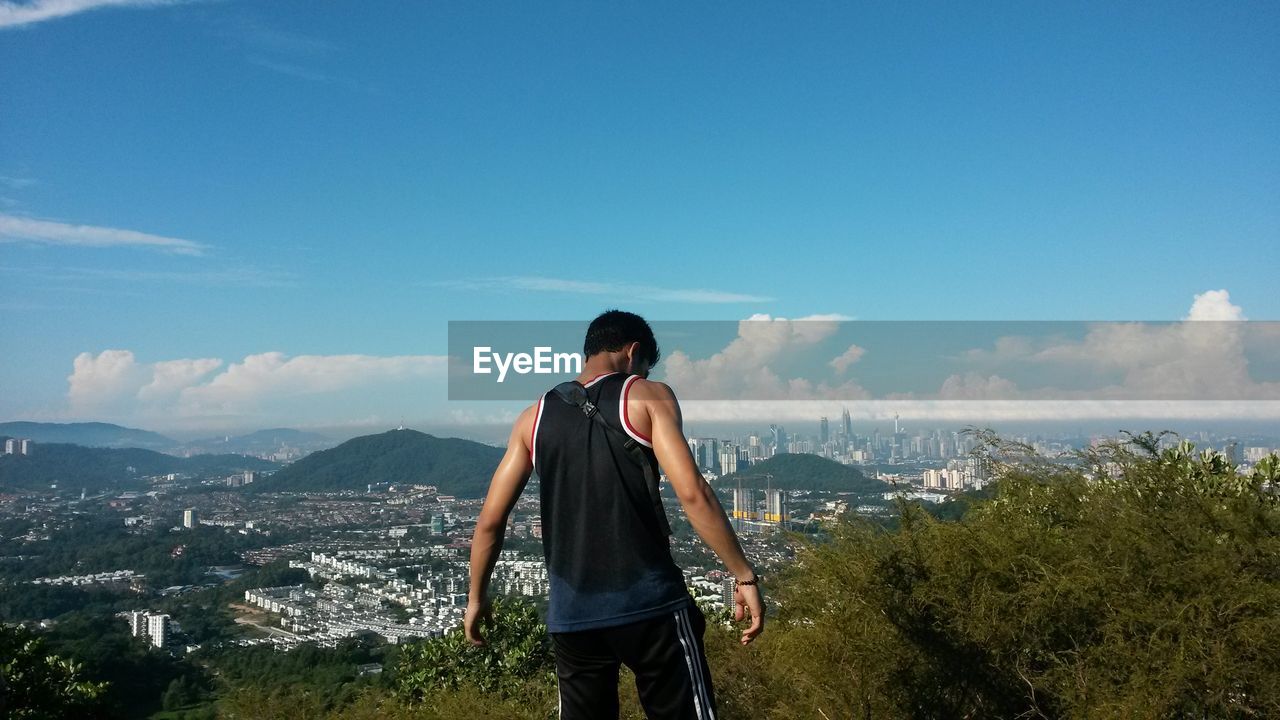 Rear view of man standing with city in background against blue sky