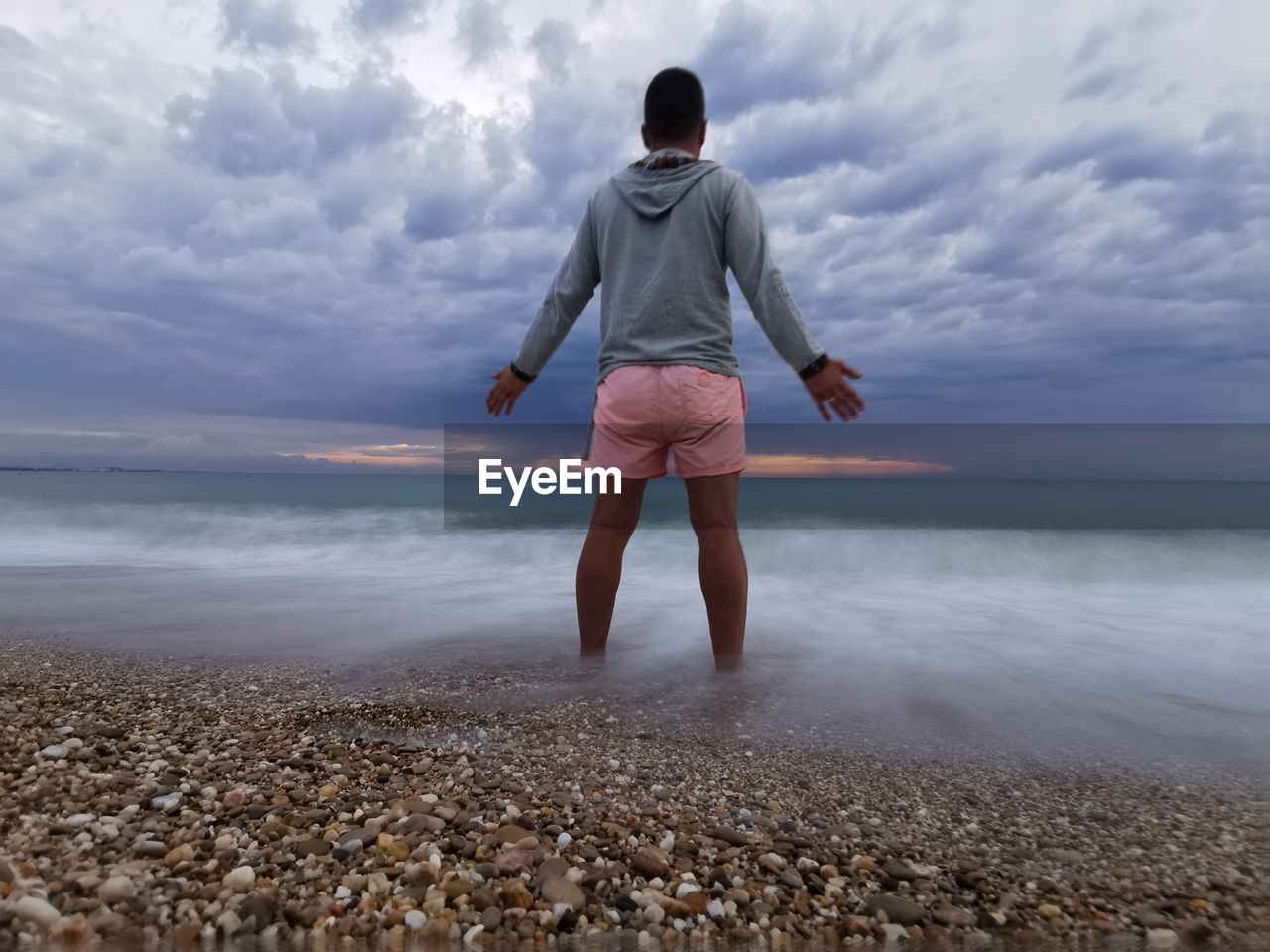 Rear view of boy standing at beach against sky