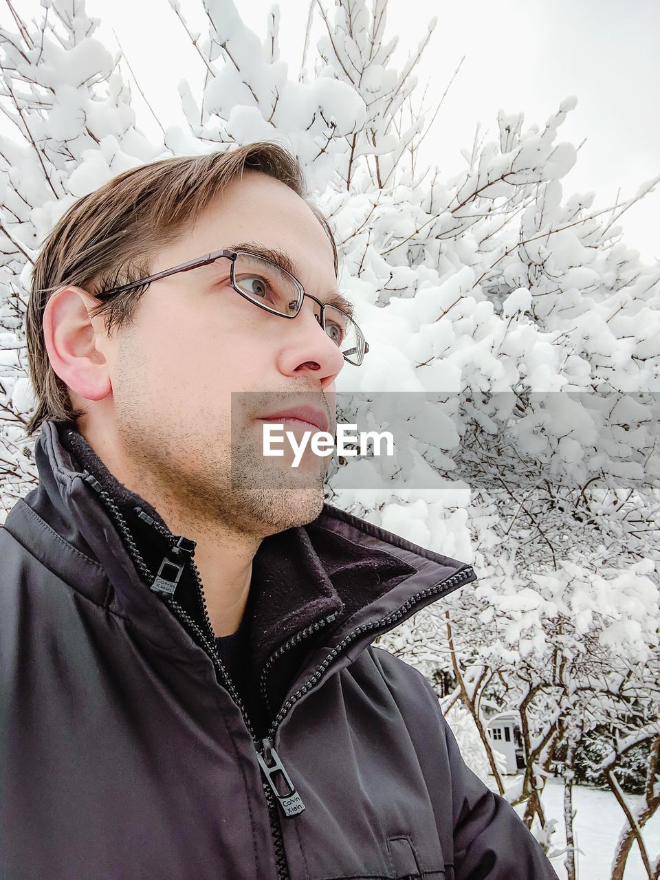 Man looking away against snowy bare trees