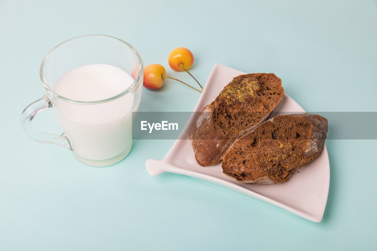 Pieces of rye bread on a white plate, next to a mug with milk on a blue background.