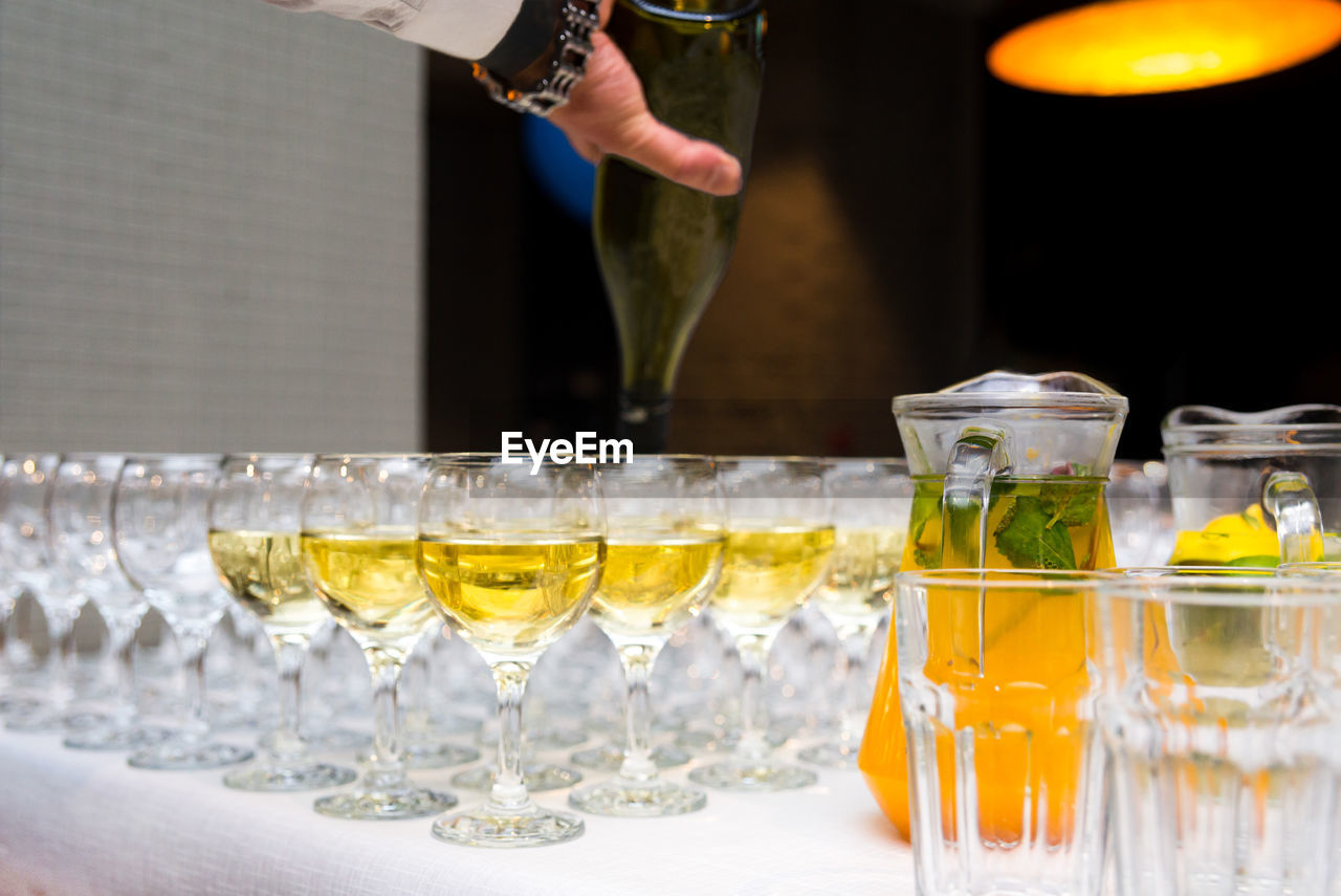 Glasses are filled with alcoholic beverages, the waiter's hand pours white wine from a bottle