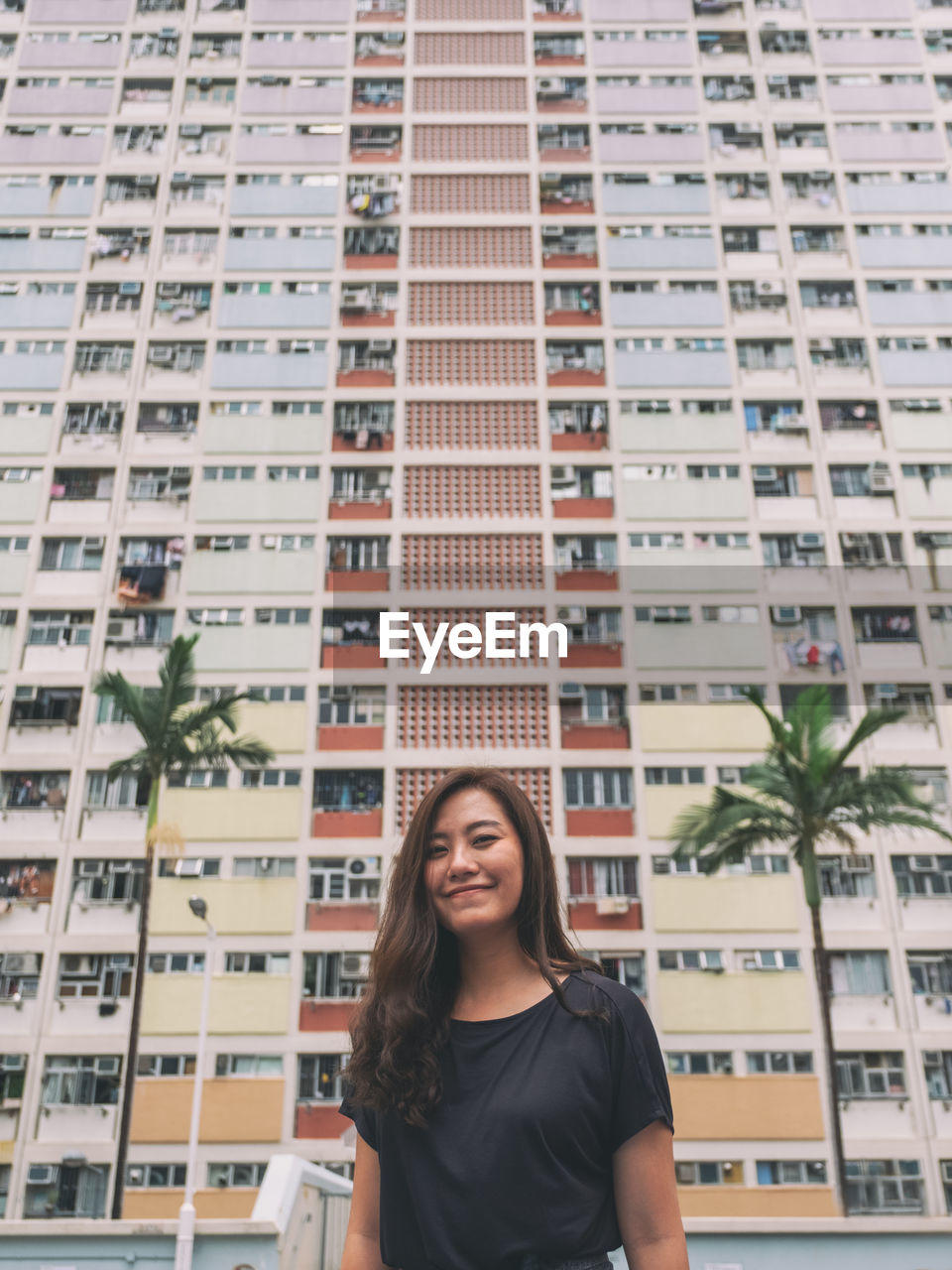 PORTRAIT OF SMILING WOMAN STANDING AGAINST BUILDINGS