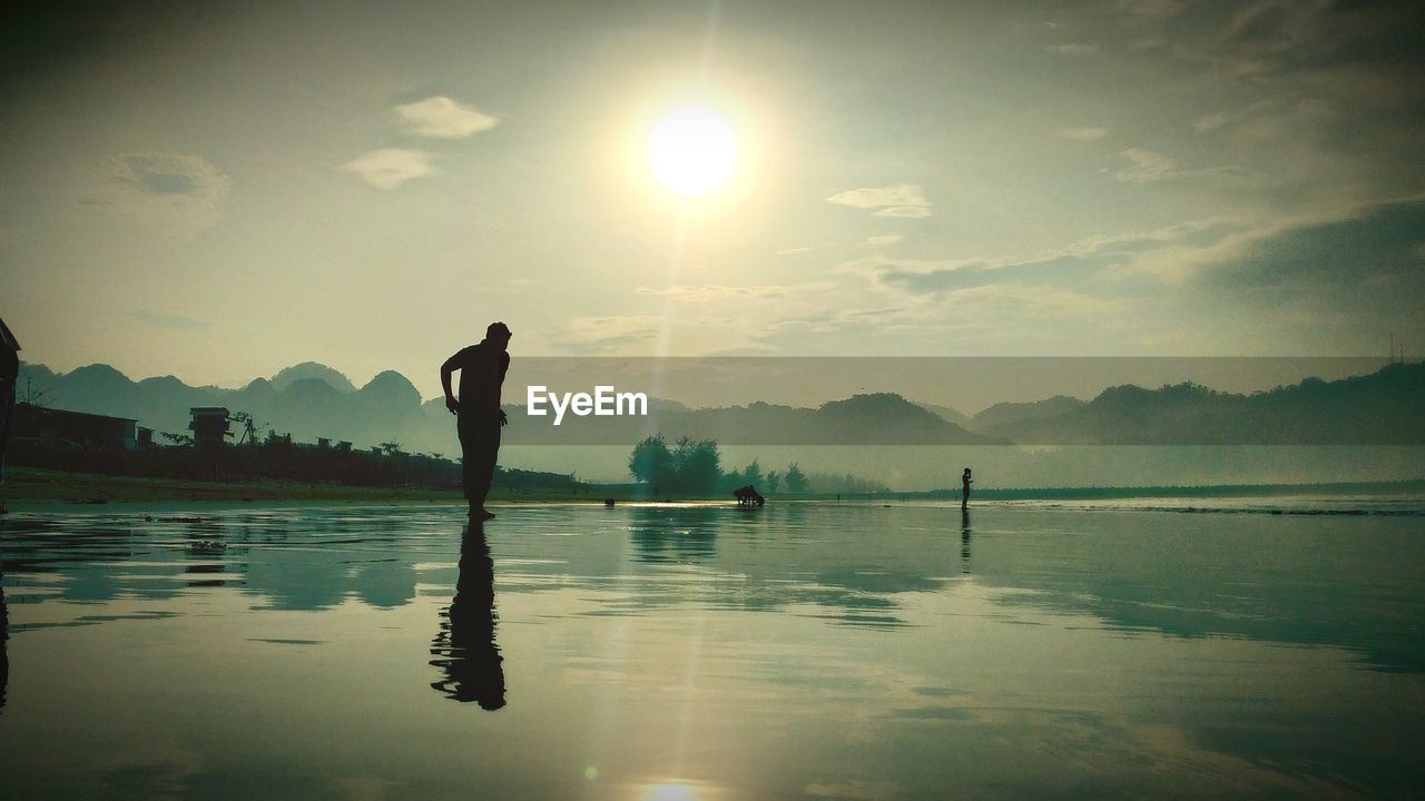 Silhouette person standing in lake against sky