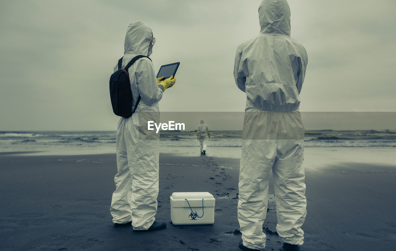 Rear view of man and woman with first aid kit standing on beach