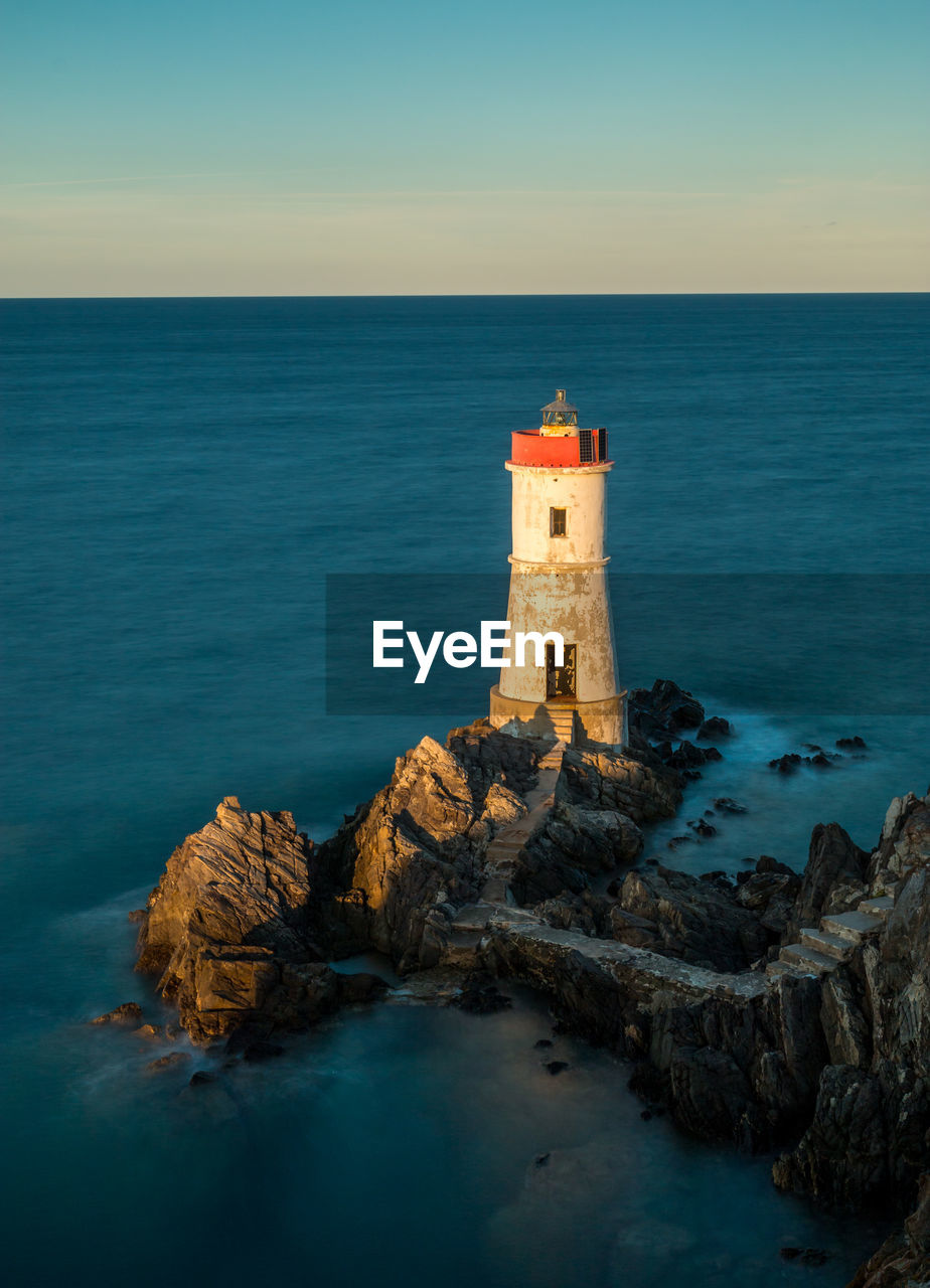 Lighthouse on rock by sea against sky