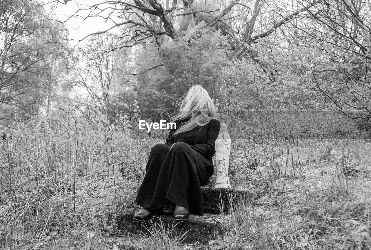 Full length of woman with statue sitting in forest