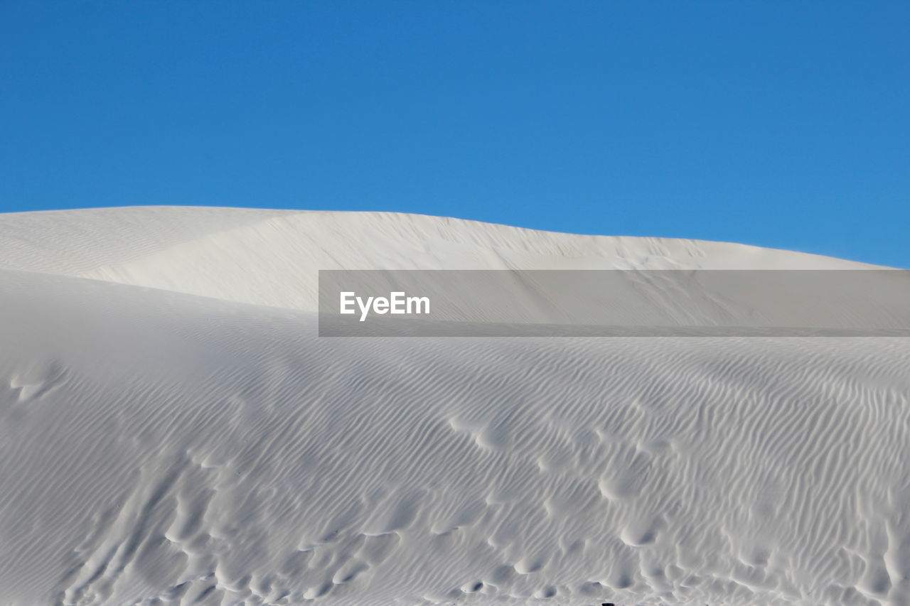 Low angle view of sand dune against clear blue sky