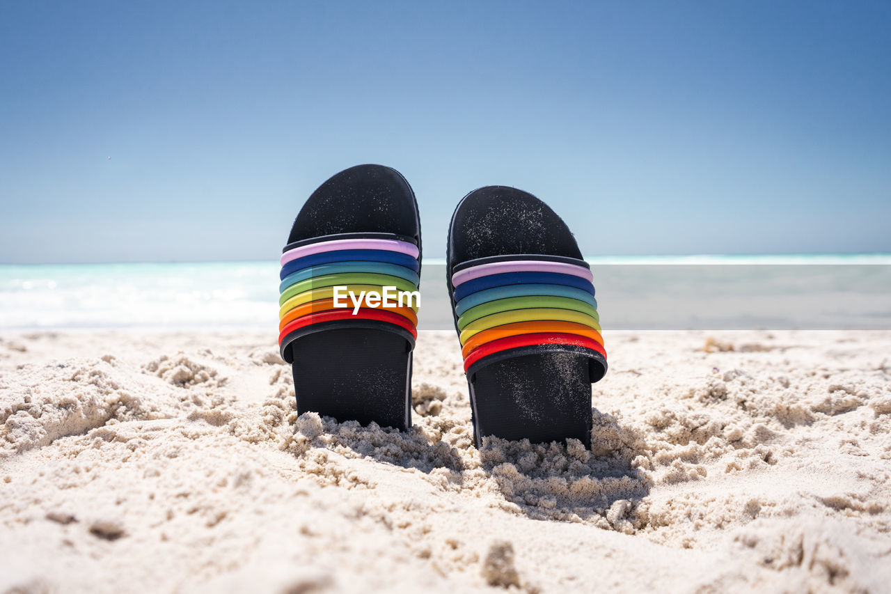 Multi colored shoes on beach against sky