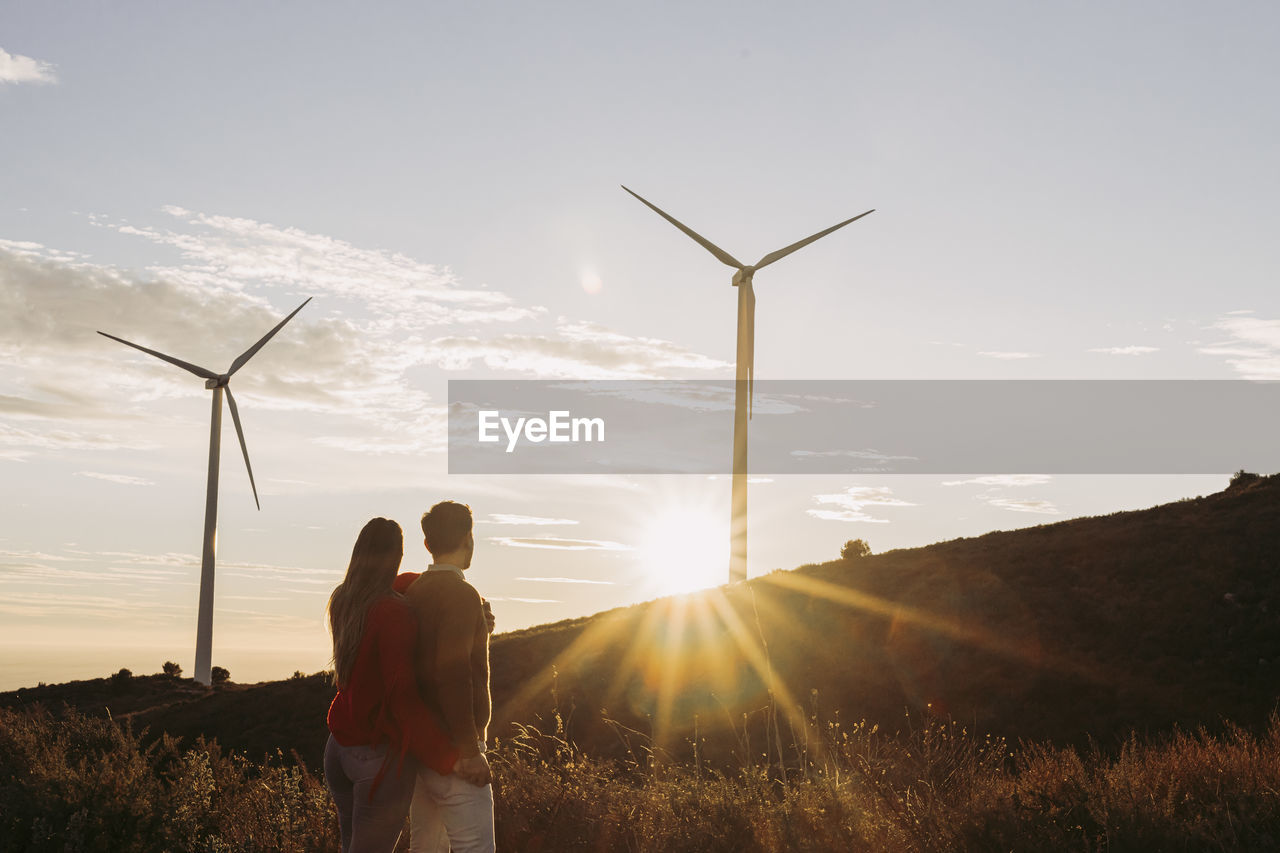 Couple holding hands looking at wind park at sunset