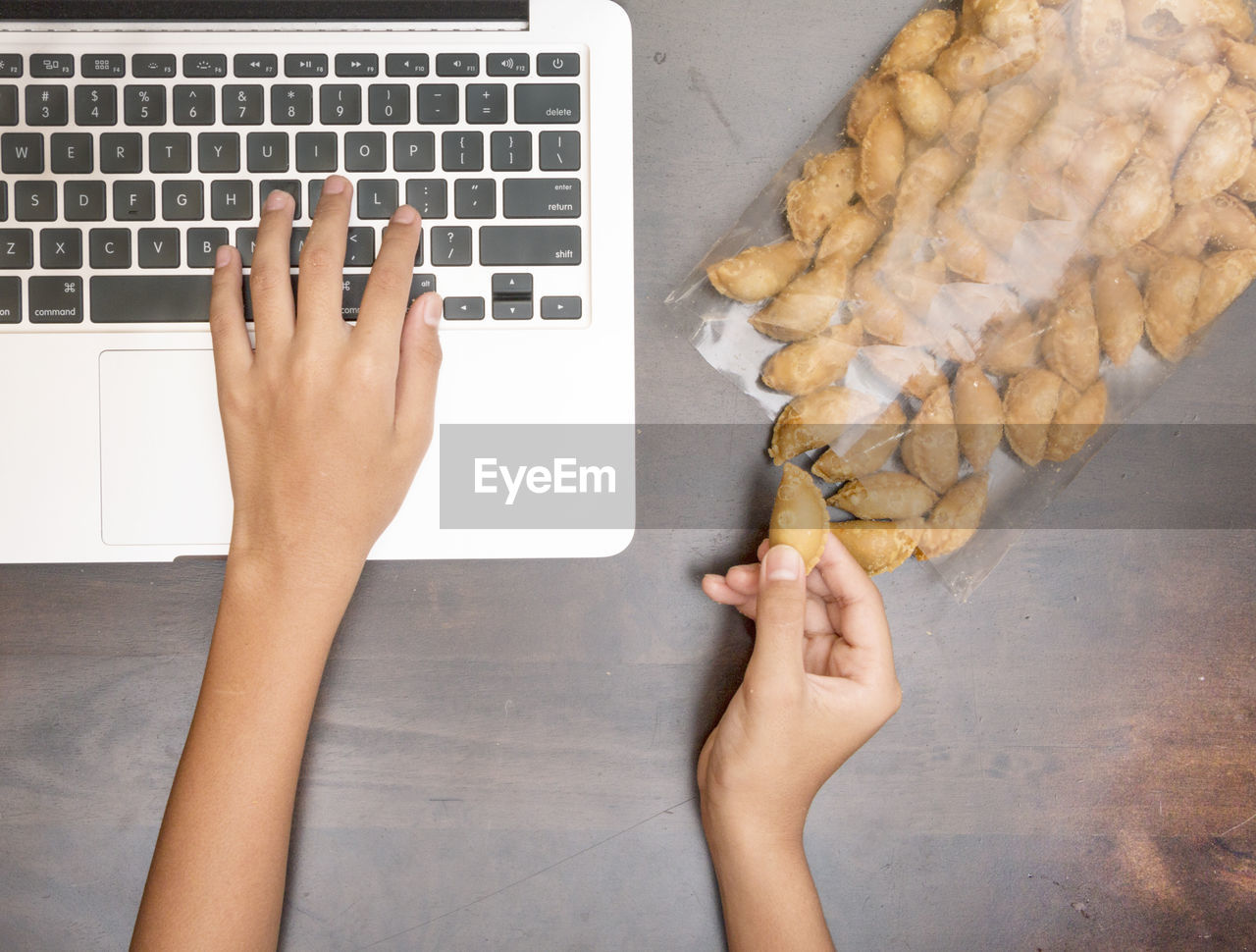 Cropped image of woman using laptop while holding snack