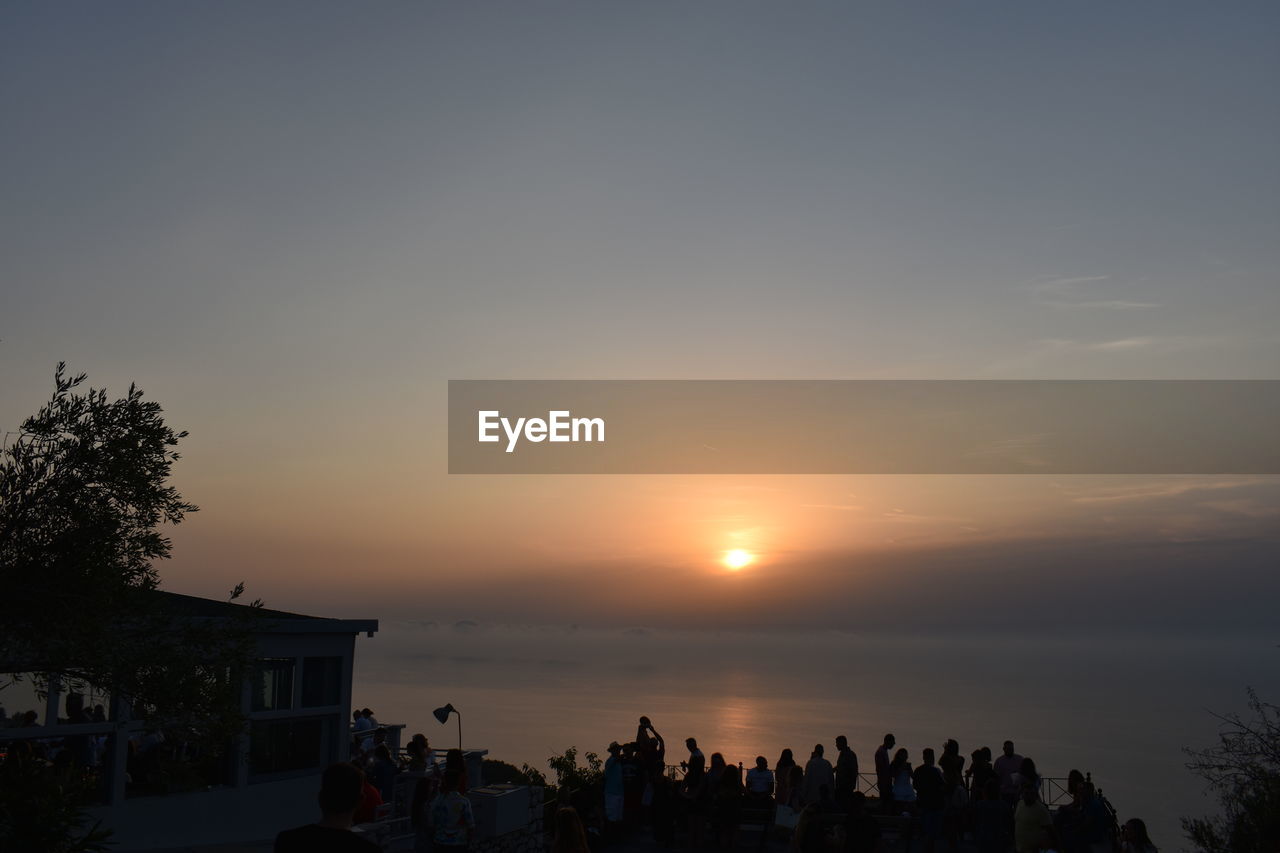 sky, sunset, evening, dusk, nature, silhouette, group of people, horizon, architecture, large group of people, crowd, water, beauty in nature, tree, sea, built structure, building exterior, cloud, plant, lifestyles, sun, scenics - nature, sunlight, leisure activity, outdoors, beach, orange color, afterglow, building, travel destinations, copy space, men, city, land, tranquility