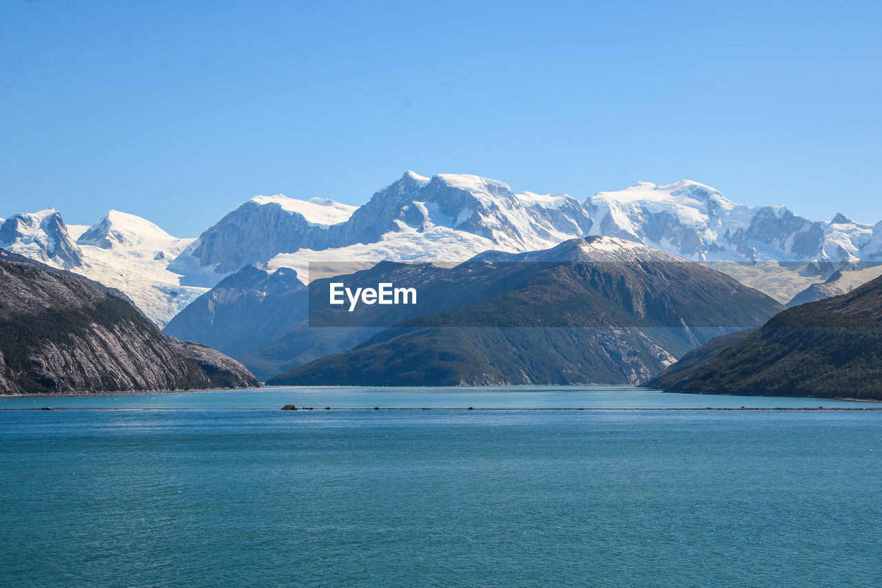 Scenic view of sea and snowcapped mountains against blue sky