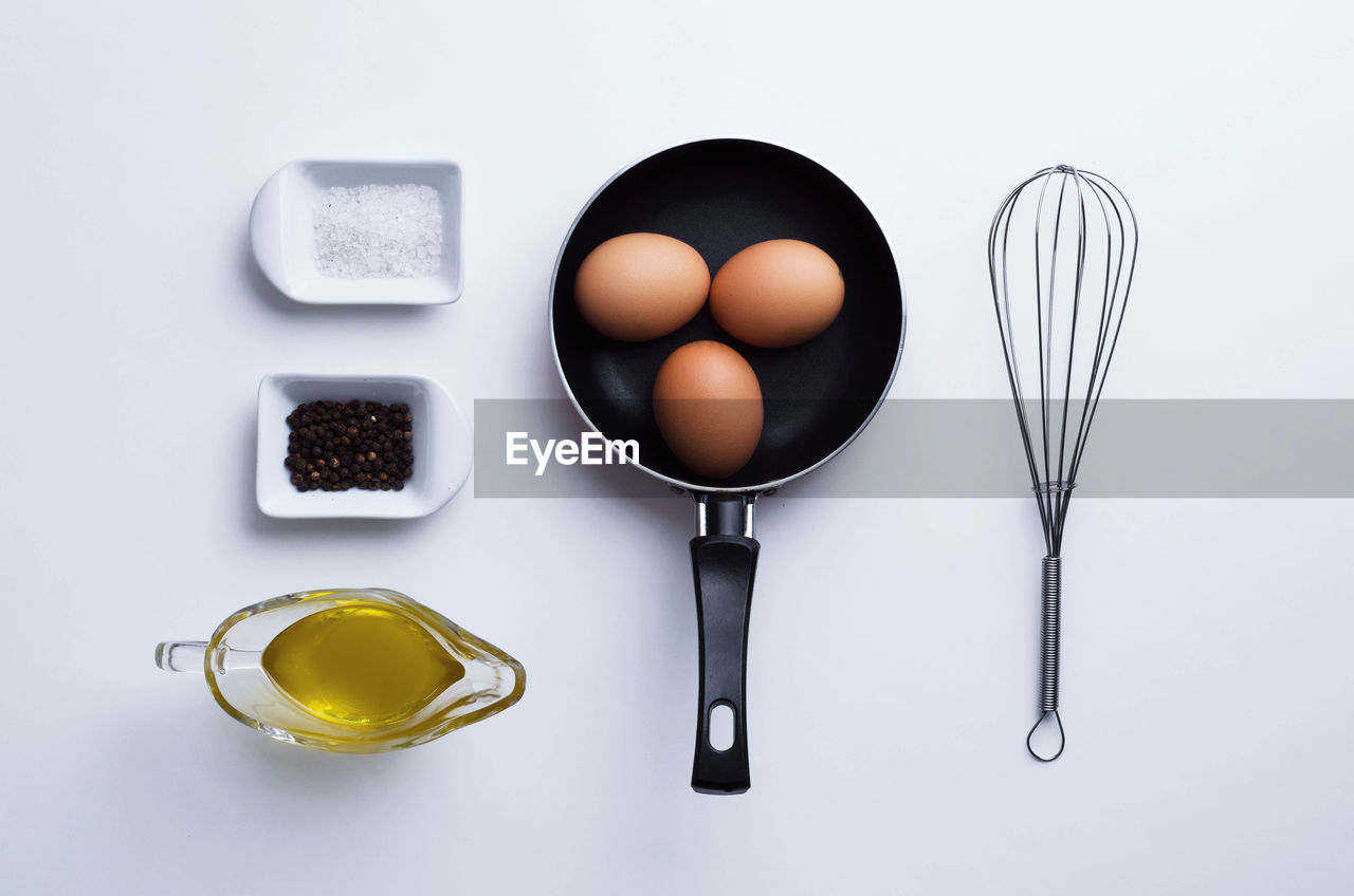 High angle view of saucepan with eggs and spice on white background