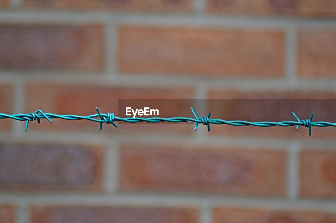 Close-up of turquoise barbed wire fence against brick wall