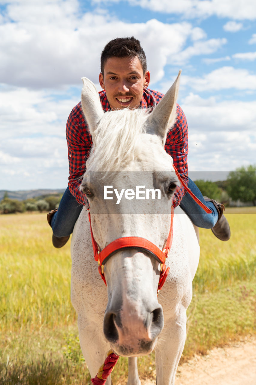 Portrait of man riding horse at ranch against sky