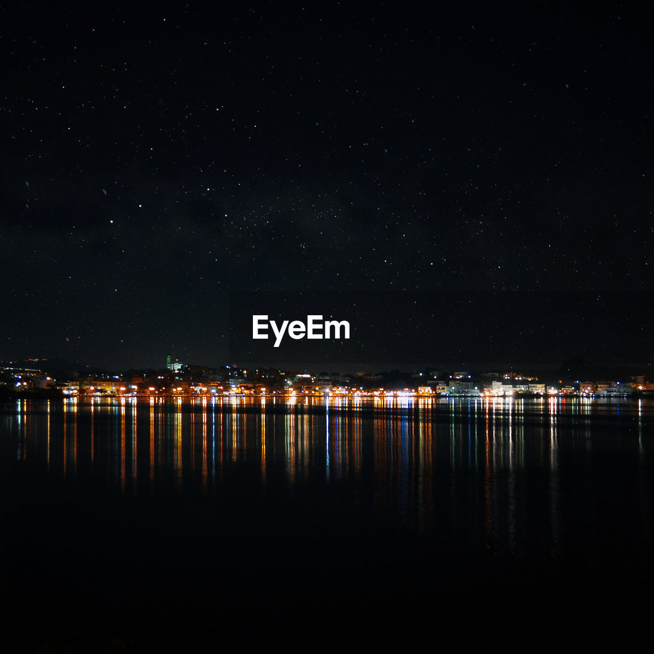 Scenic view of lake by illuminated city against sky at night