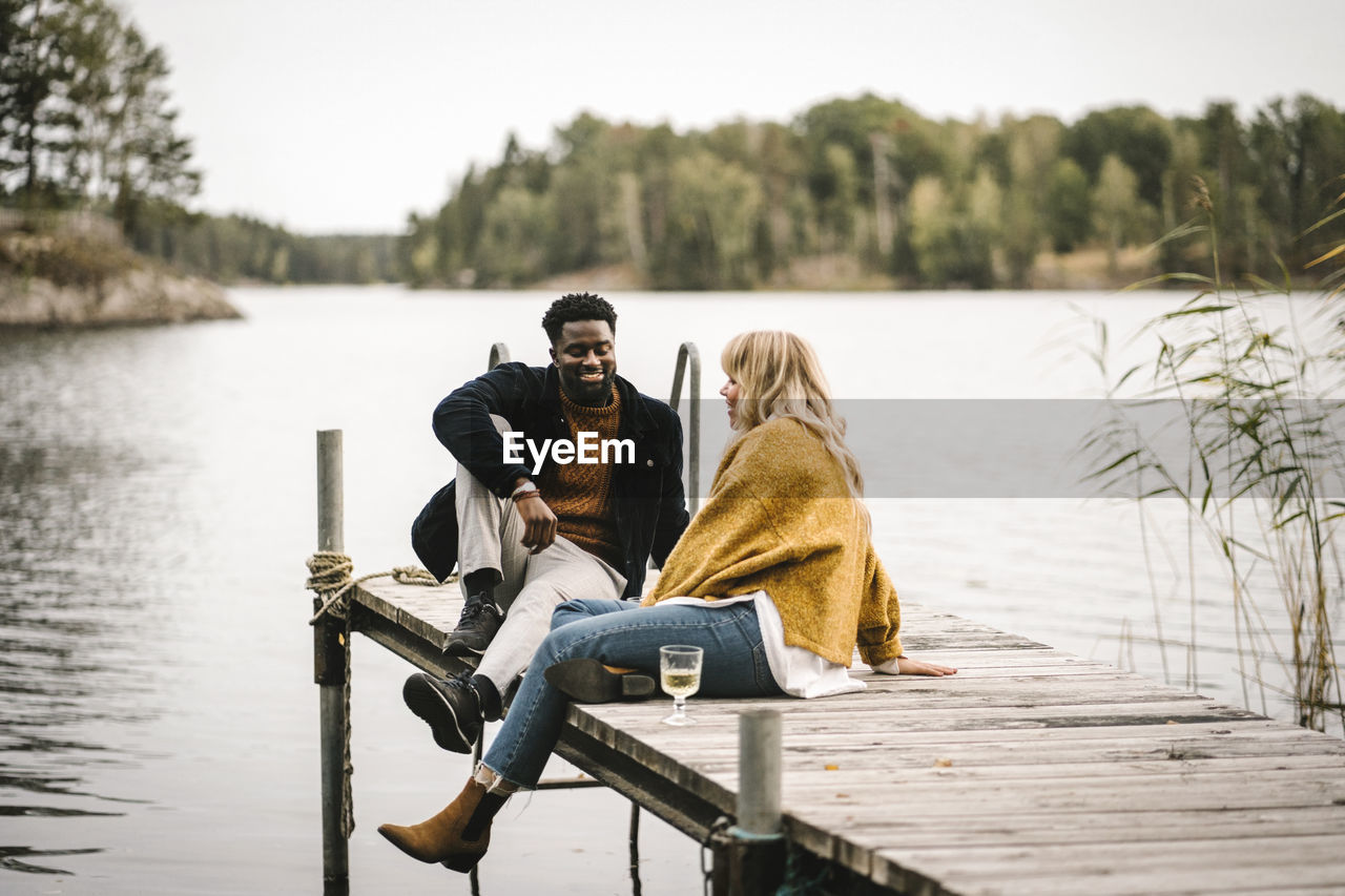 Smiling male and female partners sitting on pier over lake during social gathering