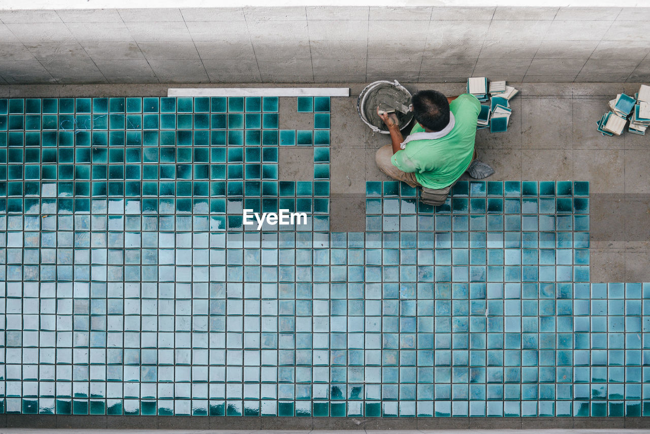 Directly above shot of workers installing tiles on floor