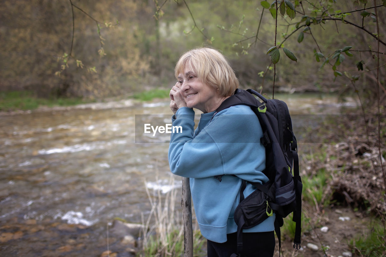 Serene elderly lady by stream in woods, a moment of tranquil reflection