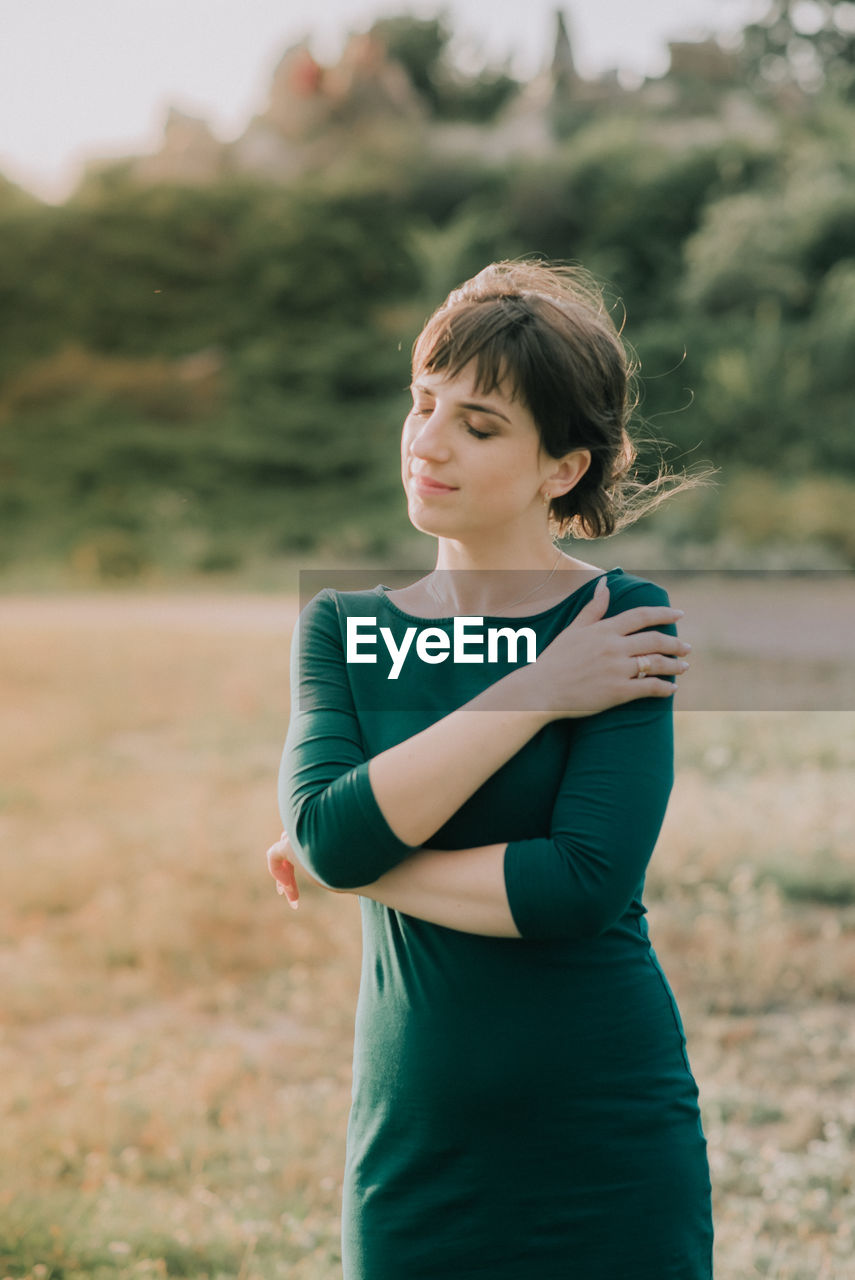 Young woman with eyes closed standing on field against plants