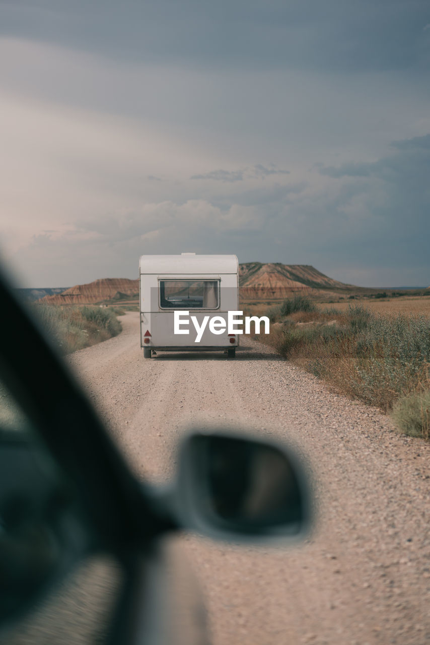 Through car side mirror view of straight roadway with caravan against mountain rural landscape