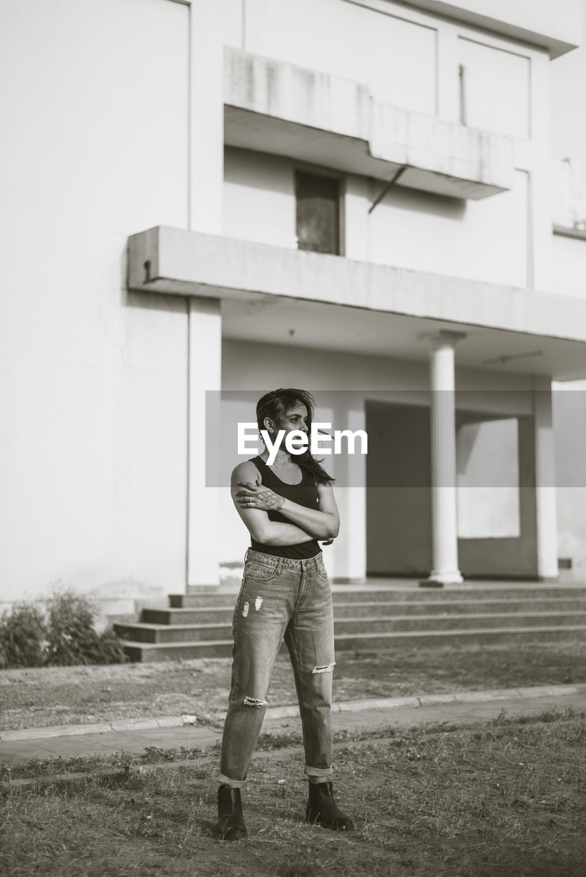 Full length portrait of woman standing on field against building