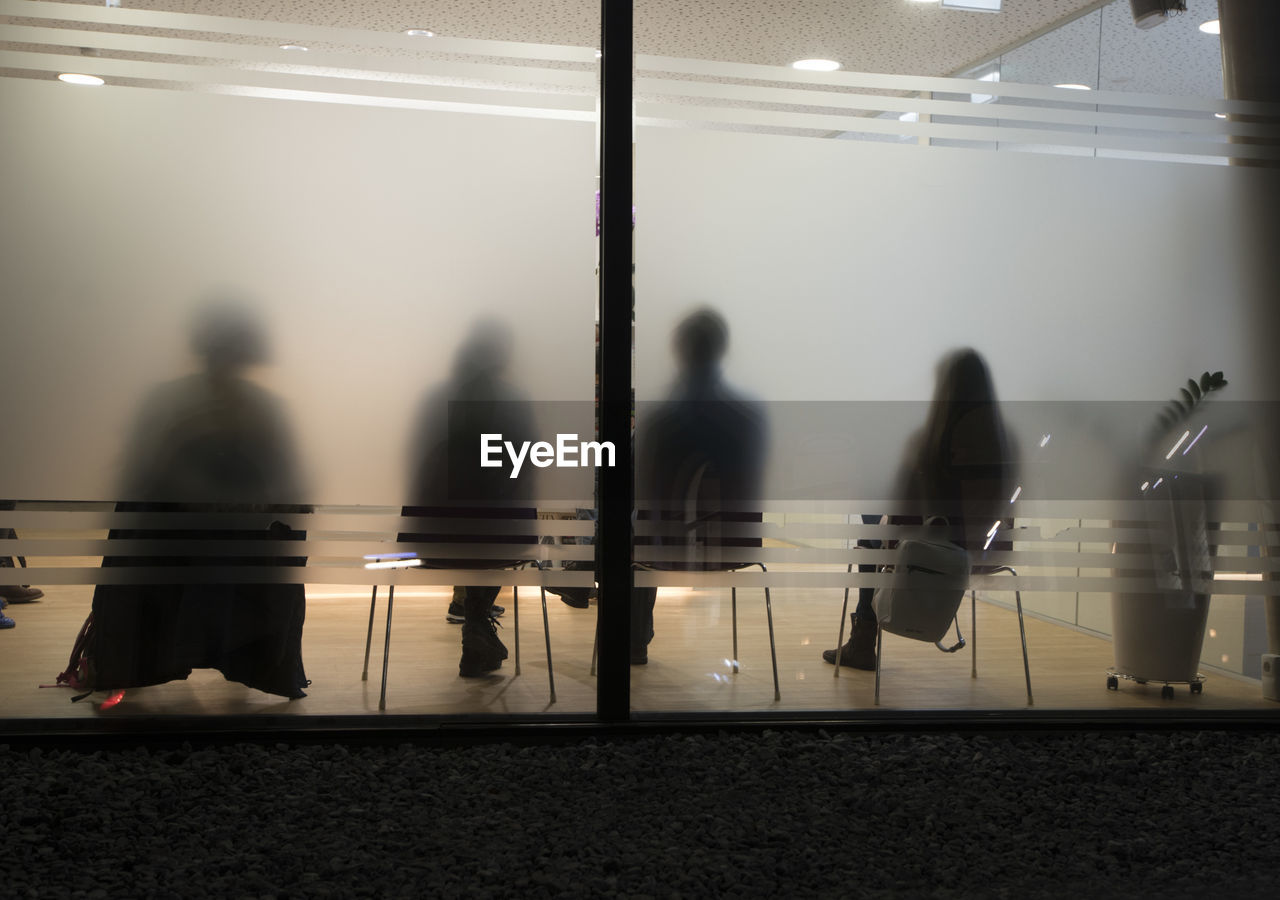 Rear view of people sitting in office seen from frosted glass wall